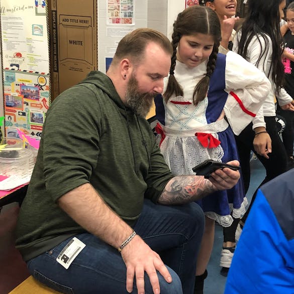  Male teacher showing young female student something on a smartphone in class 