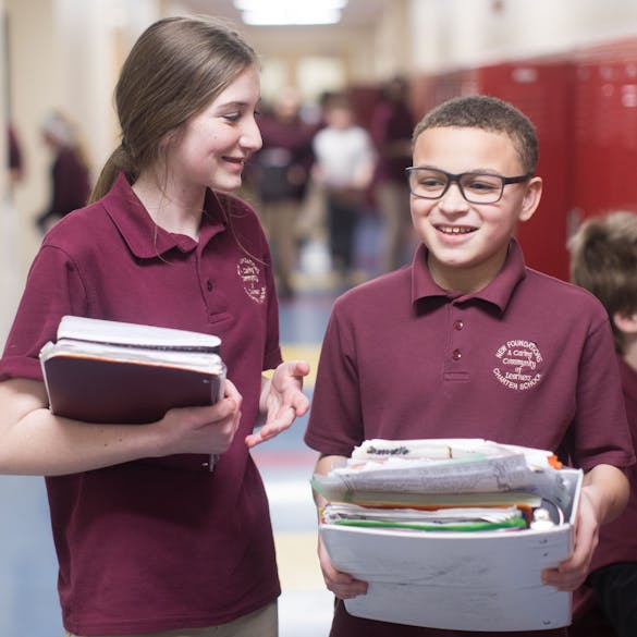  Young male and female student laughing while carrying binders in school hallway 