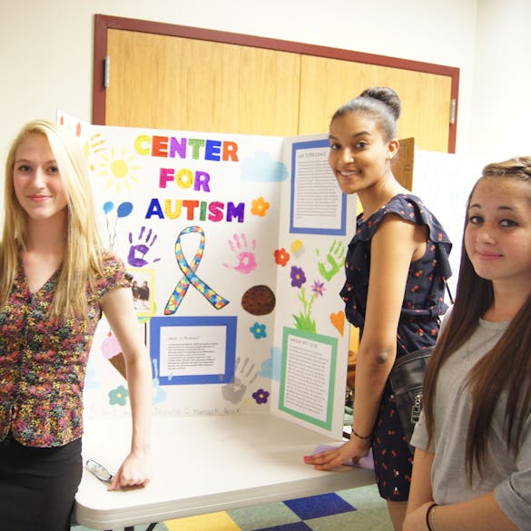  Three female students pose with a Center for Autism presentation board 