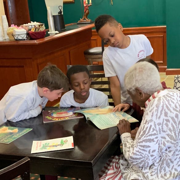 Three young male students reading a book with a senior citizen 