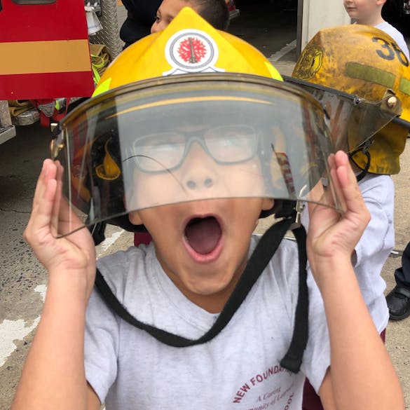  A young male student makes a silly face from under a fire fighter's helmet. 