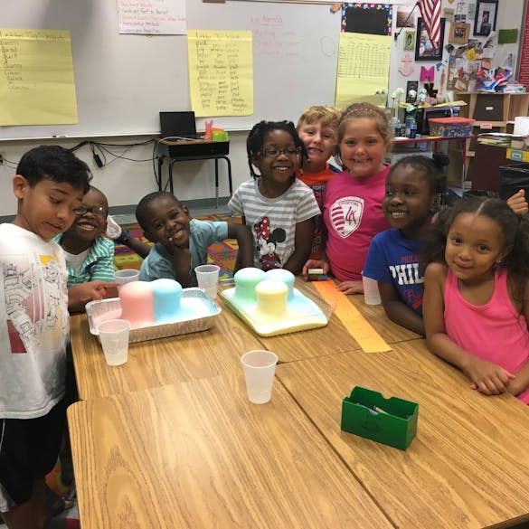  Several young students smiling at a table with colorful foaming cups 