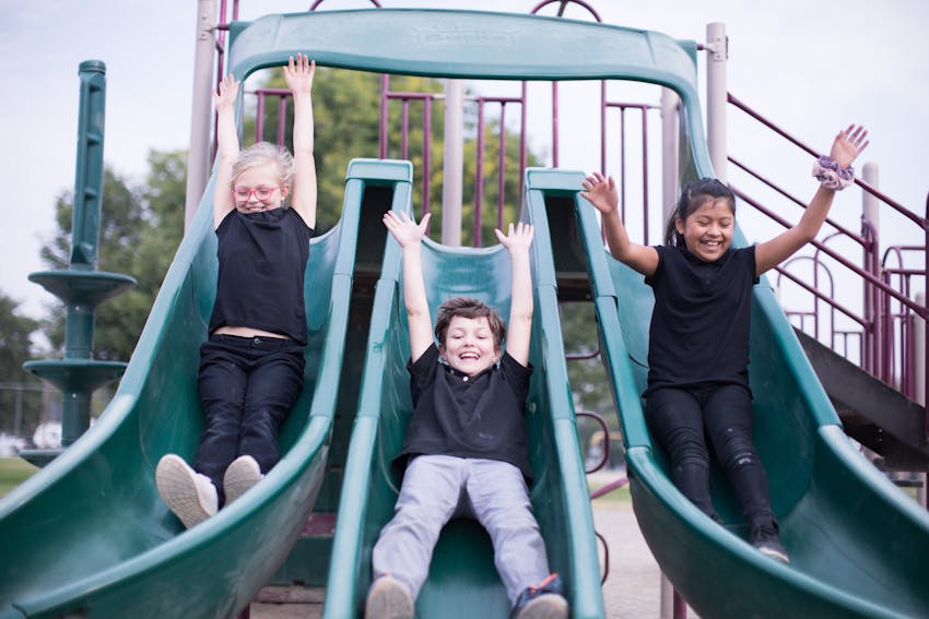 Three students sliding down a triple slide with arms in the air.